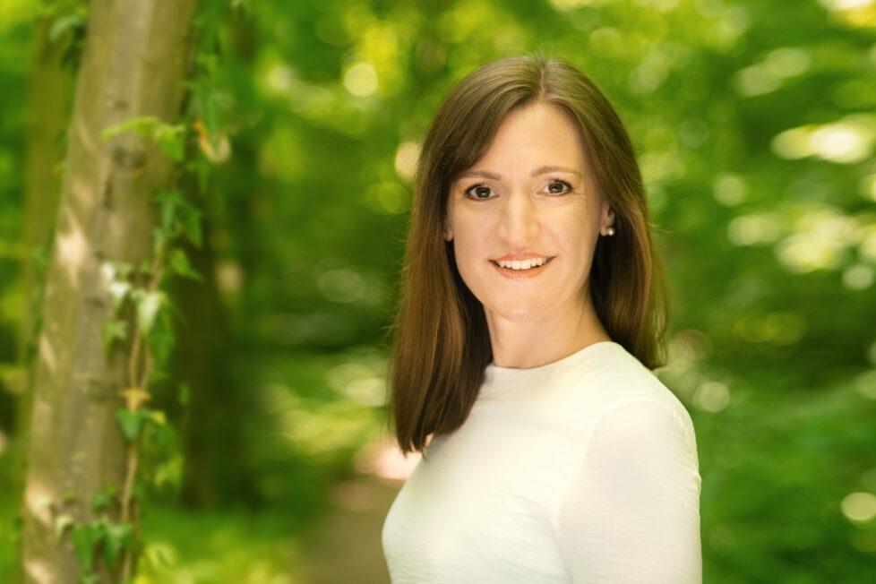 Hypnose Coachin Stephanie Konkol schaut freundlich und offen in die Kamera, im Hintergrund ein grüner Wald.