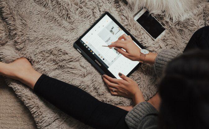 Frau in Leggins auf dem Teppich, arbeitend mit Tablet und Smartphone