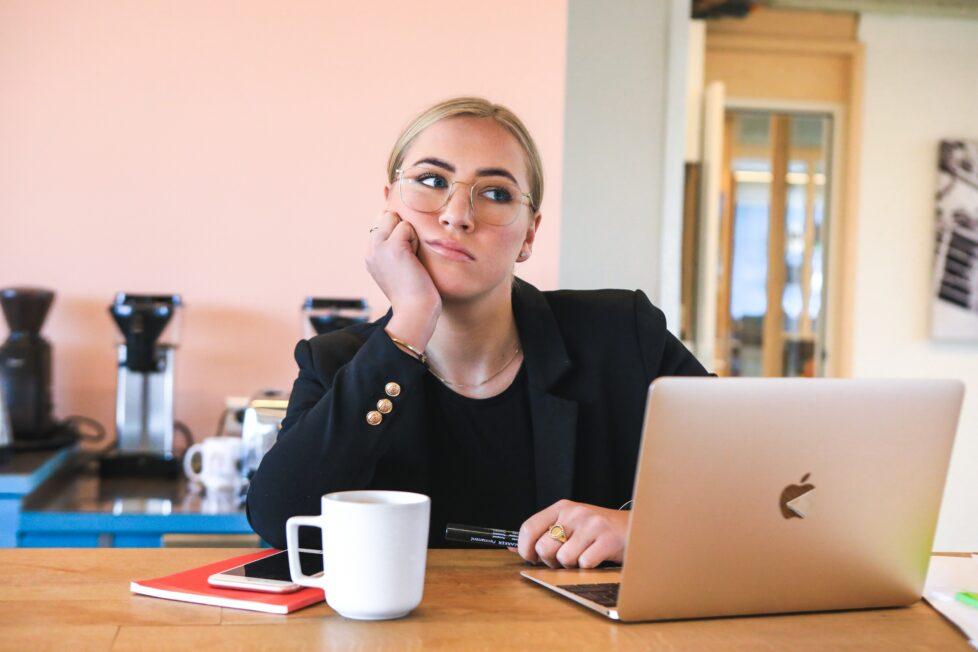 Das Bild zeigt Frau am Laptop mit Kaffee daneben, der Blick gelangweilt oder genervt, als wären Bedürfnisse unerfüllt