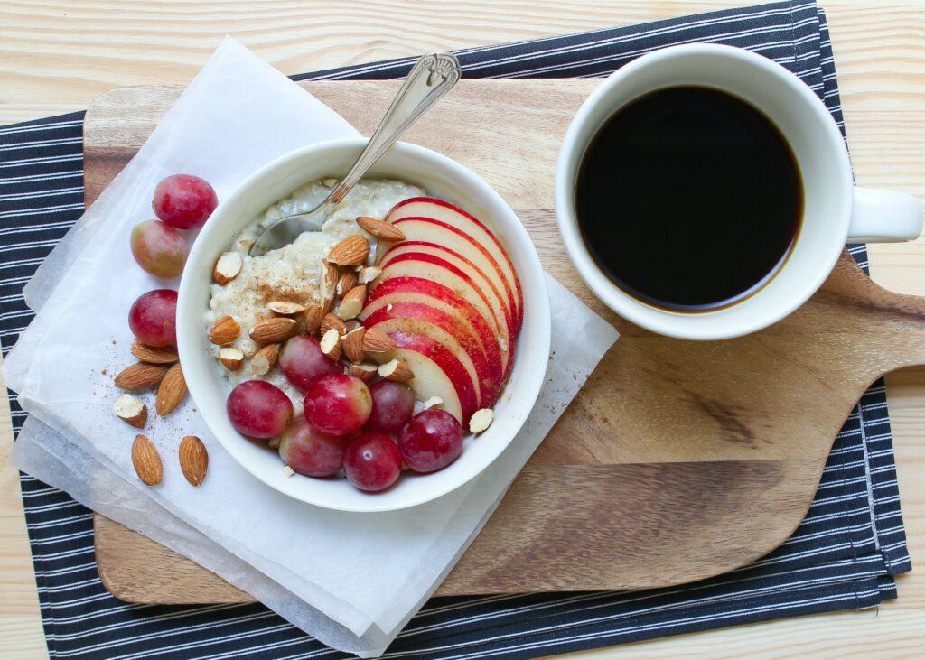 Das Bild zeigt eine Schale mit Porridge und frischen Früchten, Mandeln und einer Tasse Kaffee.