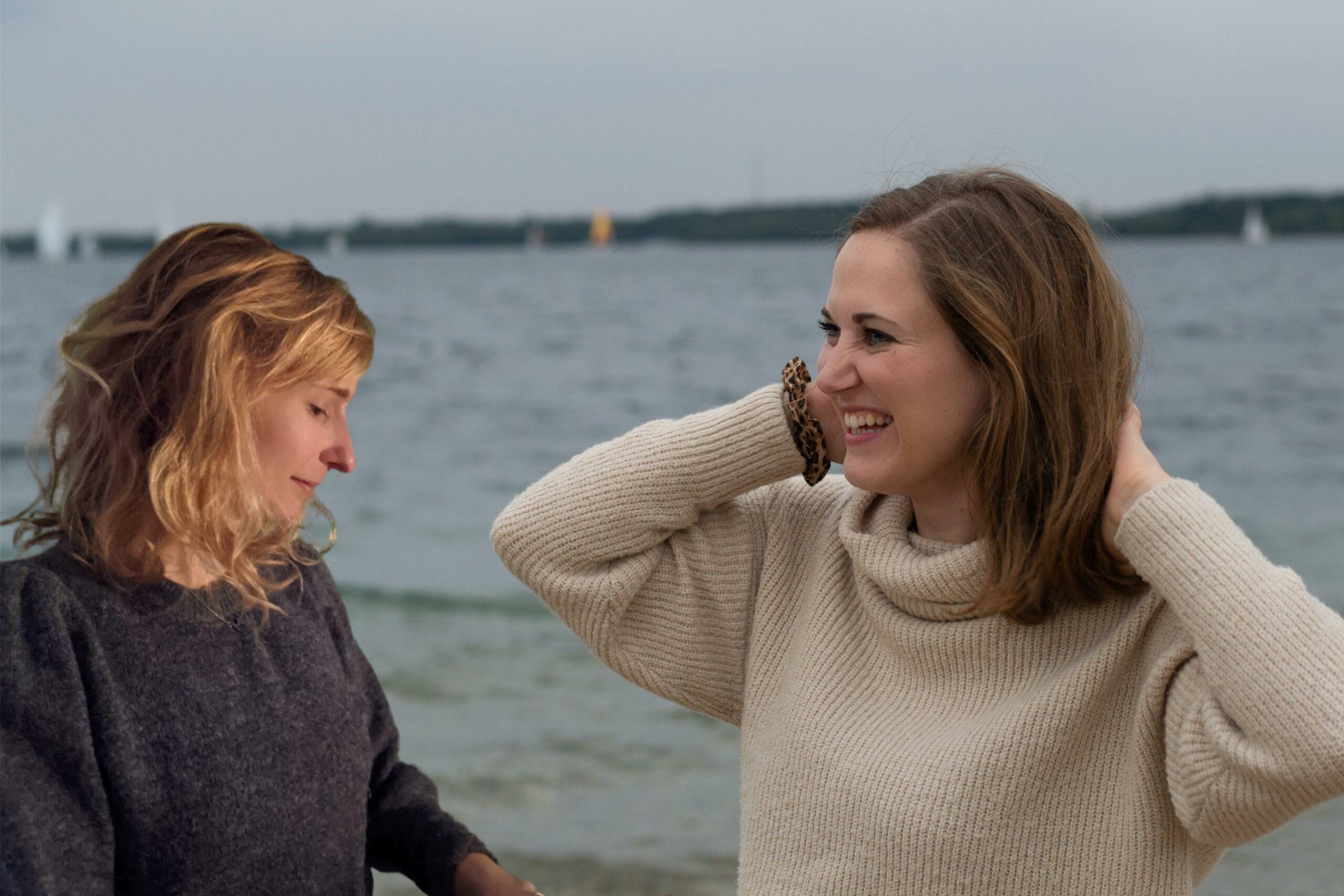 Das Bild zeigt einen Teil der Story von Anya und Fine von True Good Things. Die beiden jungen Frauen stehen dabei vor einem See und schauen sich an.