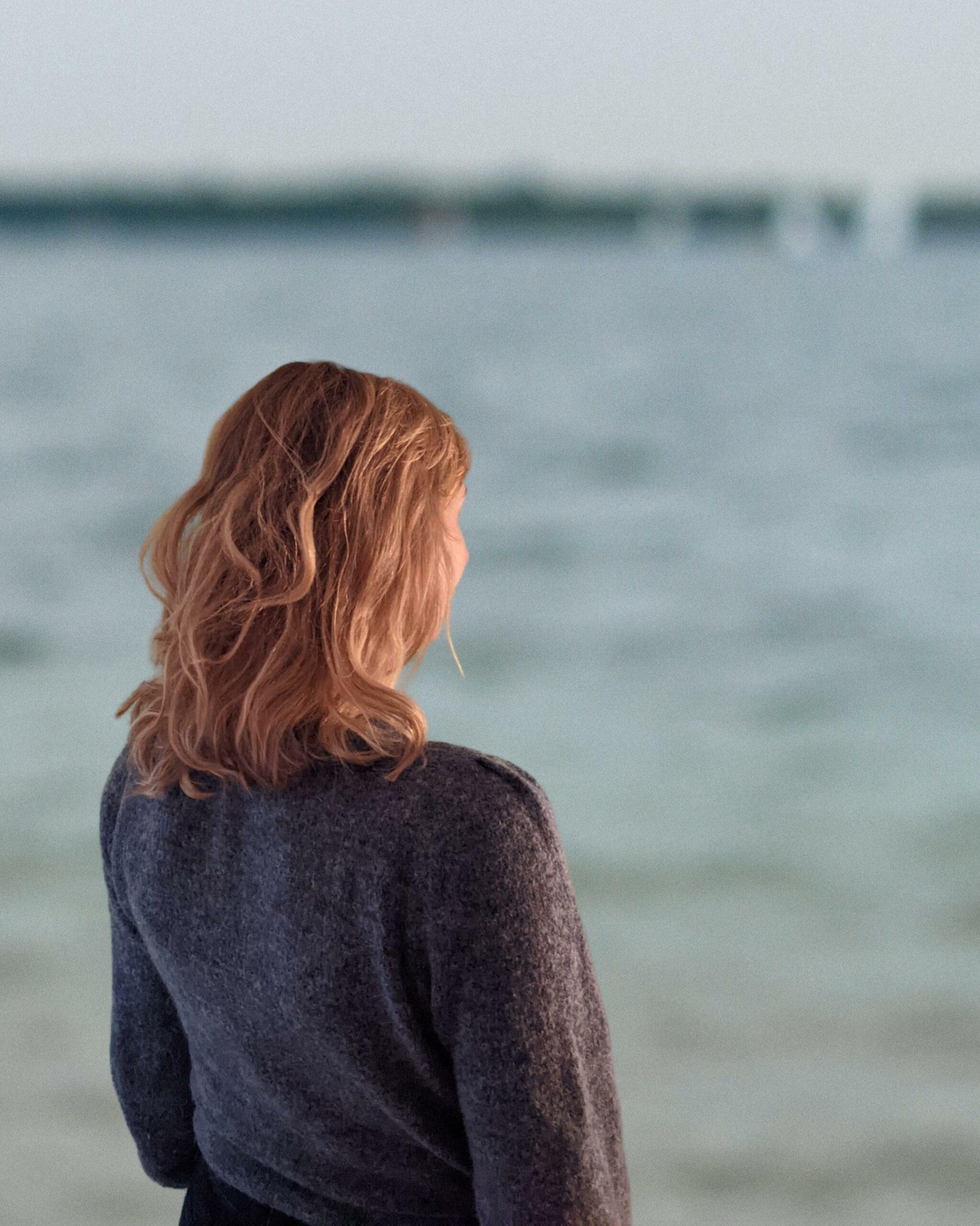Das Bild zeigt Anya, eine junge Frau mit blonden Haaren. Sie blickt auf einen See hinaus und denkt an die Story von True Good Things.