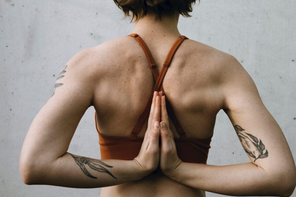 Das Bild eine Frau von hinten mit verschränkten Händen in der Yoga Pose Namaste.