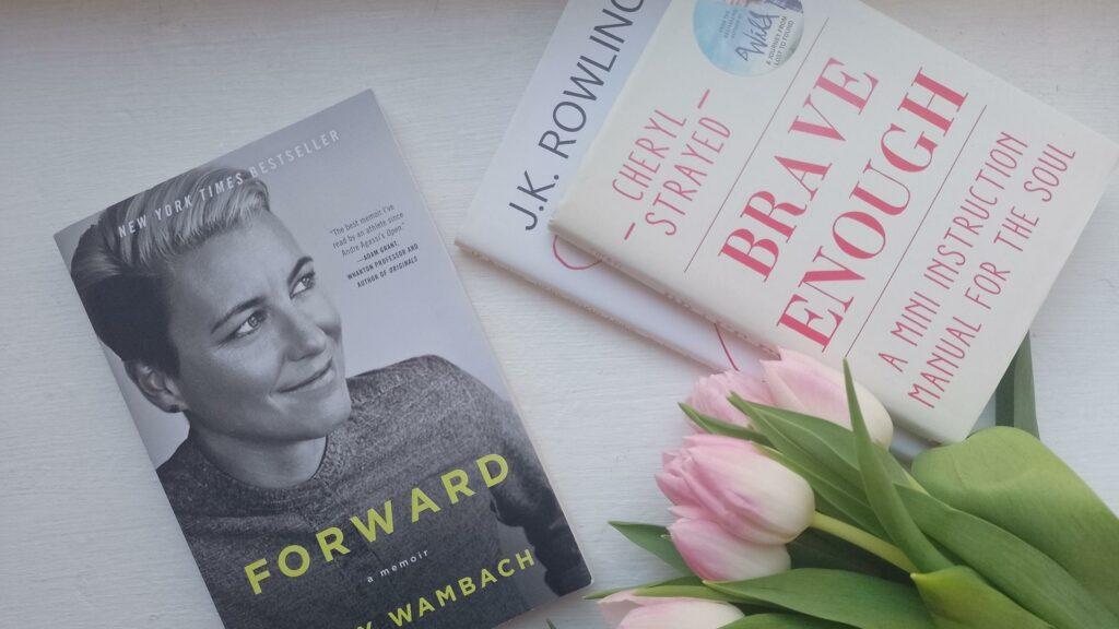 Das Bild zeigt einen Stapel Bücher, daneben das Buch Forward von Abby Wambach und ein Strauß pinker Tulpen.