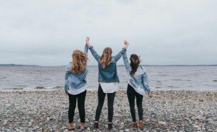 Das Bild zeigt drei Frauen am Meer, die vor Freude die Arme in die Luft heben und das Ankommen und Weitermachen von True Good Things feiern.
