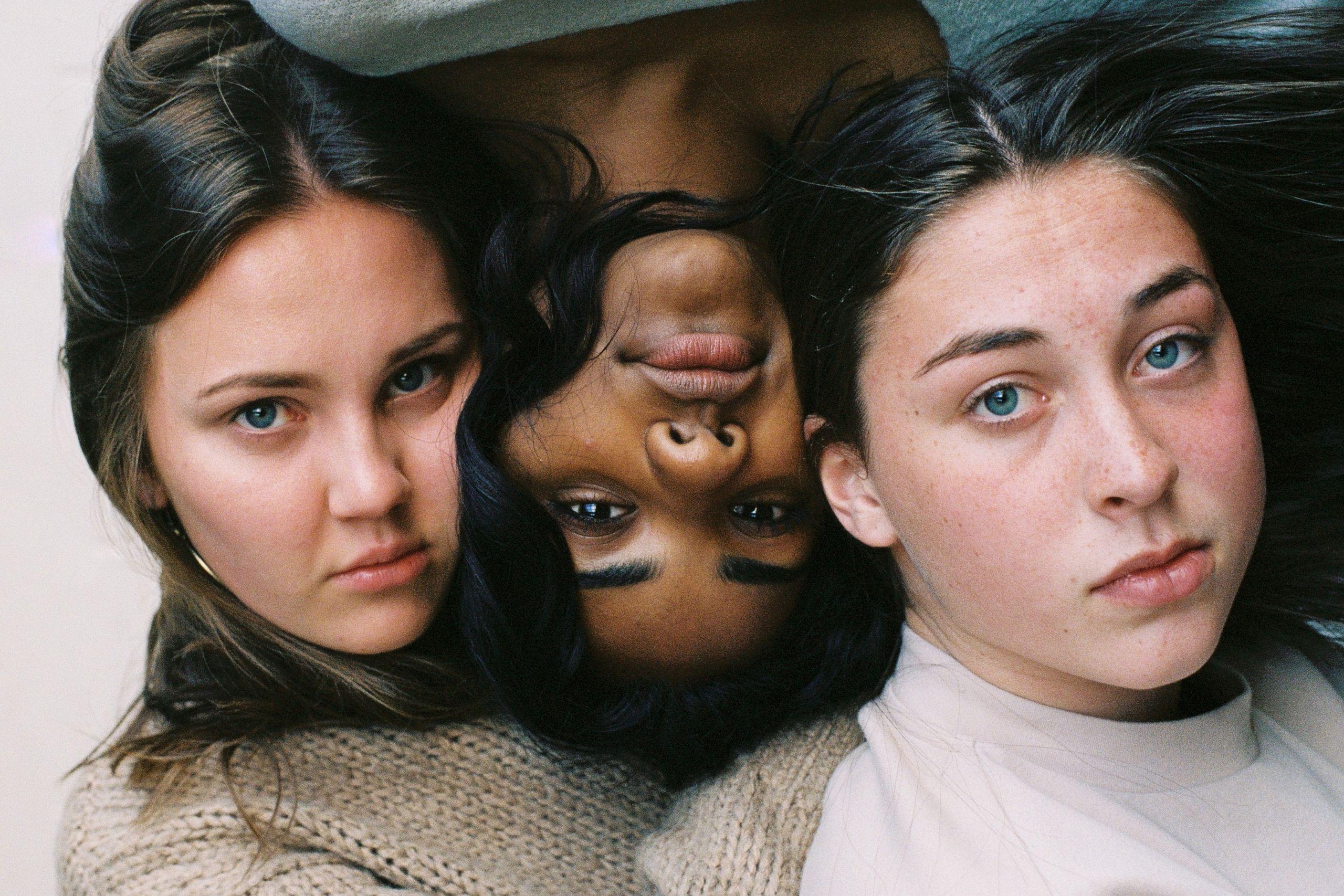 Das Bild zeigt drei Frauen die ernst in die Kamera blicke und das Thema Selbstoptimierung in Frage stellen.