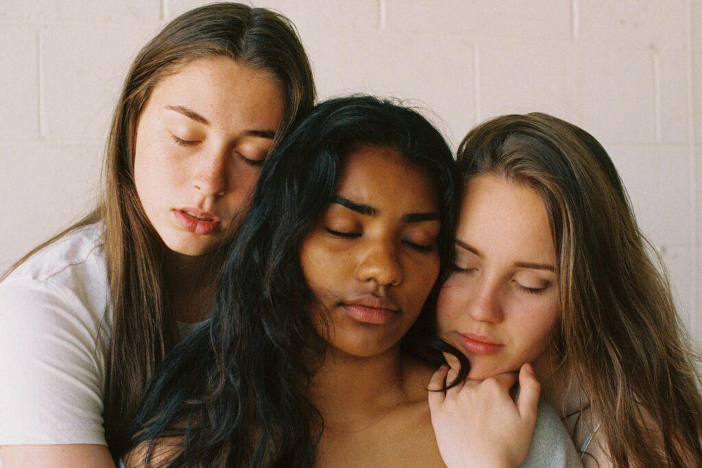 Das Bild zeigt drei Frauen mit geschlossenen Augen und sich mit dem Thema Selbstoptimierung auseinandersetzen.